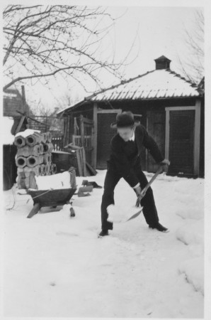 Pappa skottar snö iklädd kostym och hatt